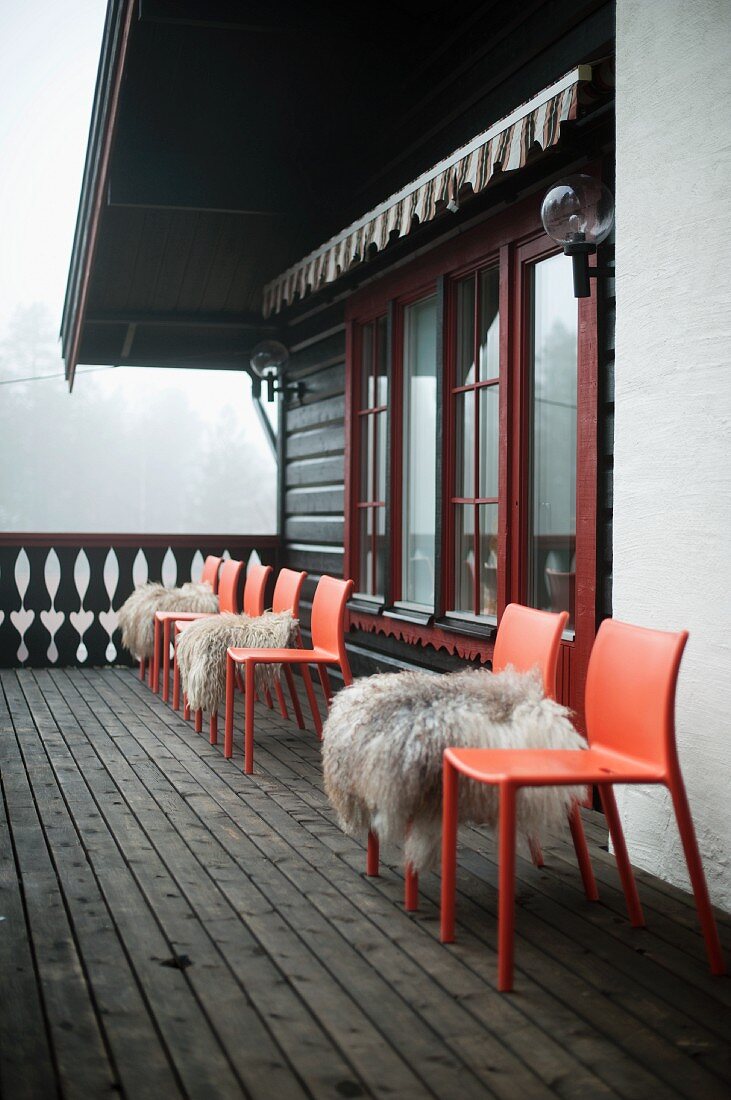 Rote Kunststoffstühle mit Tierfellauflage auf Balkon vor Holzhütte