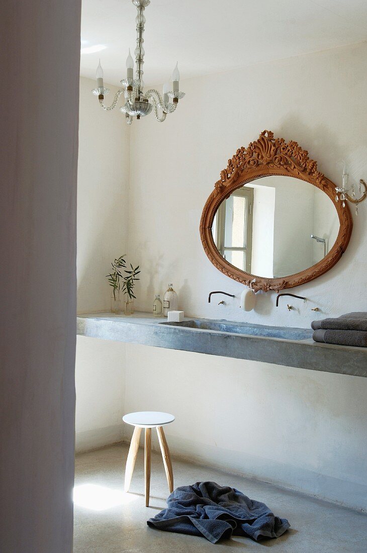 Antiker Ovalspiegel über schmalem Beton Waschtisch, zierlicher Hocker und Kristallüster in provenzalischem Bad