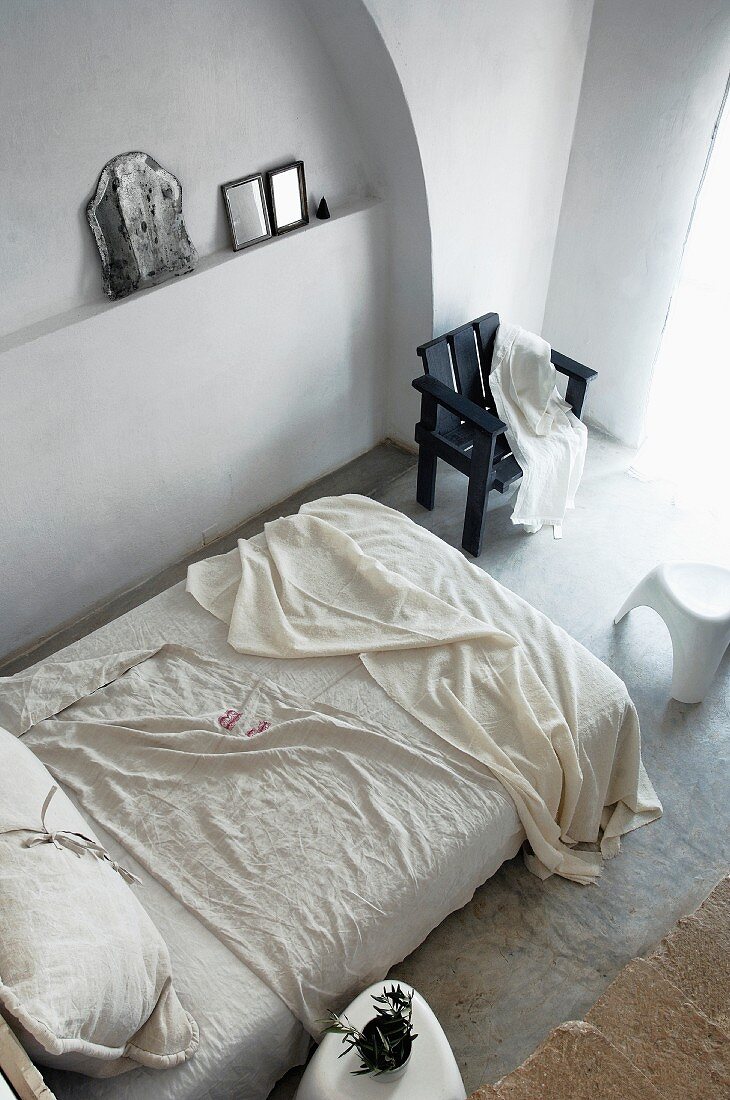 Französisches Bett und schwarzer Stuhl vor schlicht dekorierter Wandnische in mediterranem Schlafraum