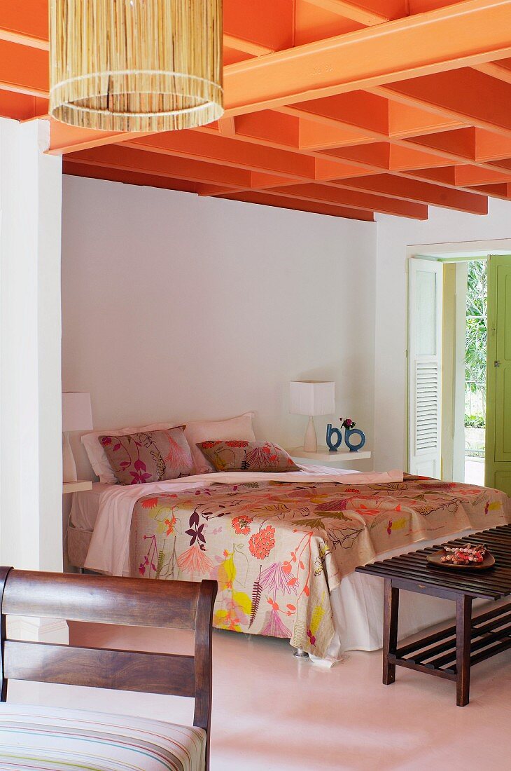 Orangerot gestrichene Deckenkonstruktion über Doppelbett mit floral gemustertem Bezug