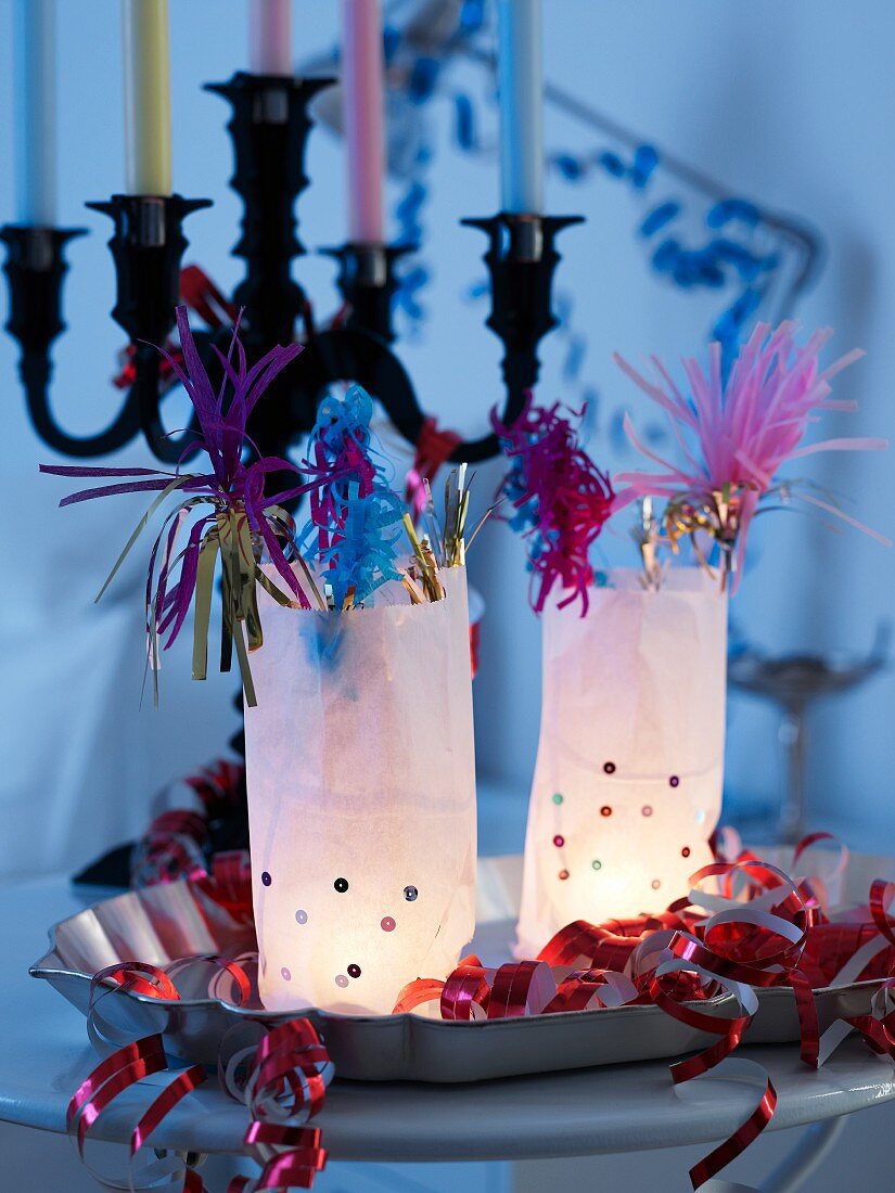 Beleuchtete Tüten mit Partydeko auf Metallschale vor mehrarmigem Kerzenständer