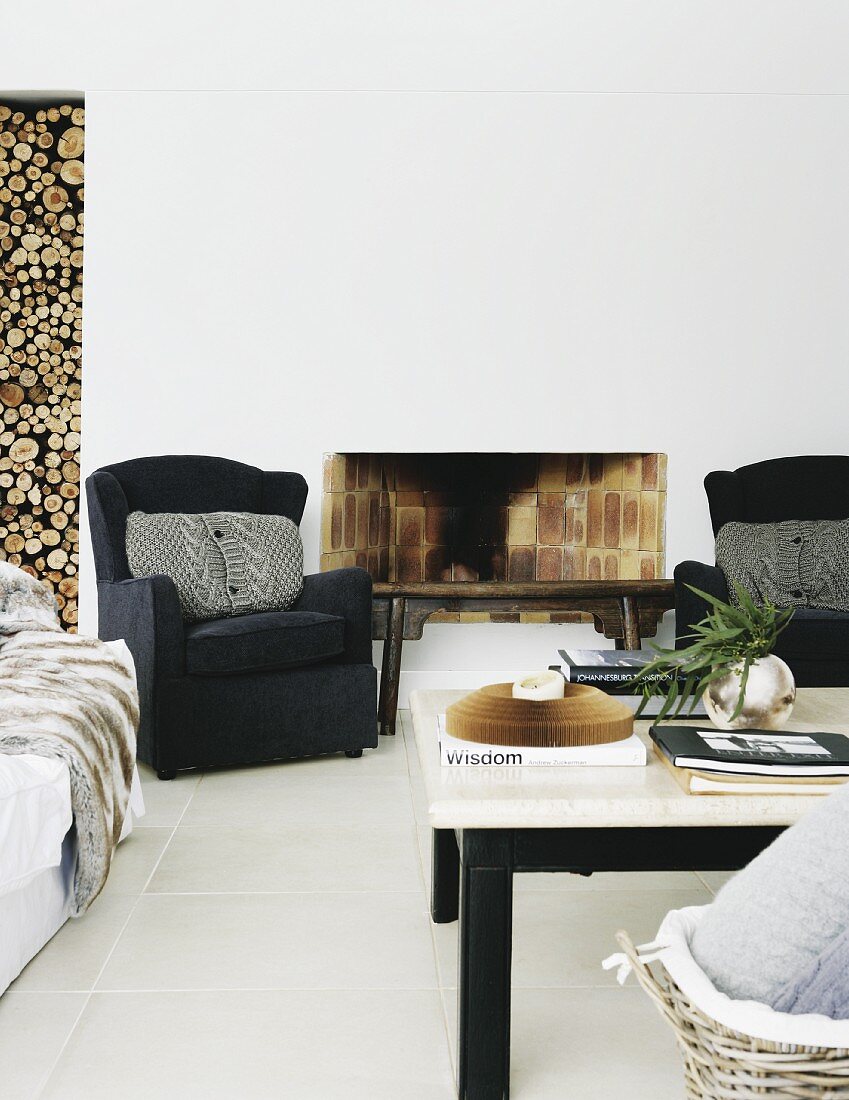 Seating group on white tile floor in front of an open brick fireplace and wall niches with stacked firewood