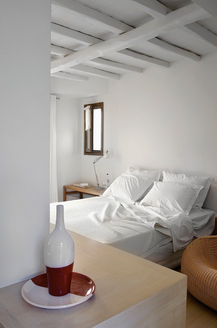 Double bed in simple bedroom; red and white ceramic plate and bottle