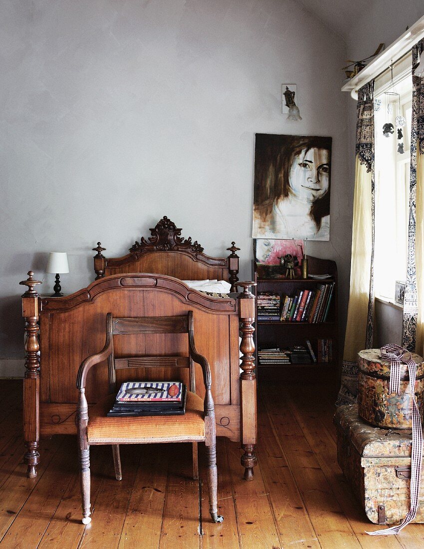 Antiker Holzstuhl vor Schlittenbett aus geschnitztem Holz und modernes Portrait an Wand in schlichtem Ambiente