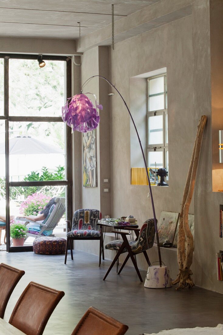 Kleiner Tisch mit Stühlen im Retrostil und Stehlampe mit flippig violettem Schirm vor raumhoher Fensterfront im Loft