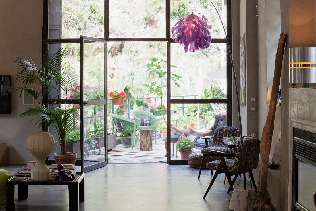 Künstlerischer Möbel- und Objektemix im Loft vor Fensterfront mit Blick auf begrünte Terrasse