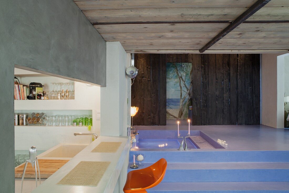 Orange bar stool at kitchen counter in front of dramatic, lavender blue bathroom landscape with sunken spa tub and romantic mural