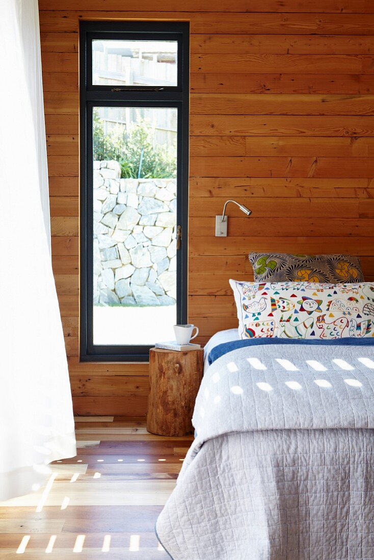 Doppelbett an holzverkleideter Wand neben Fenster