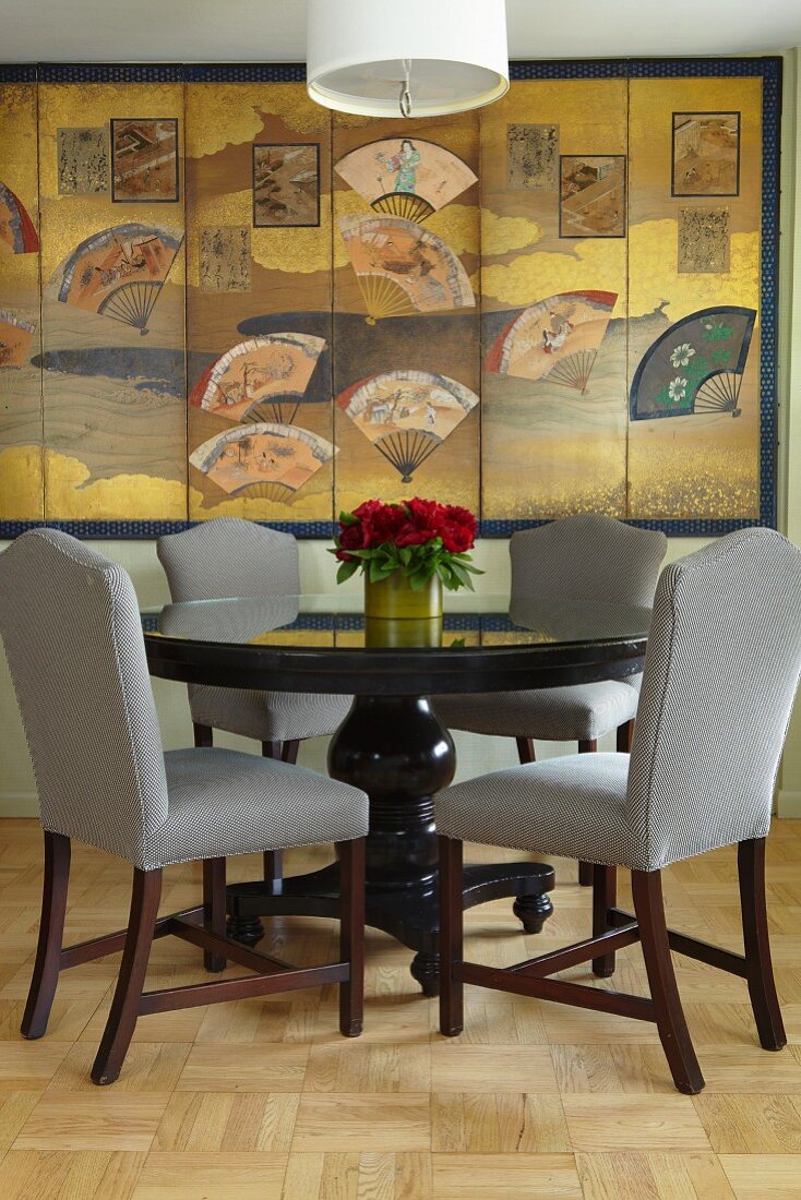 Upholstered chairs at round dining table in front of large-scale artwork with Oriental motifs