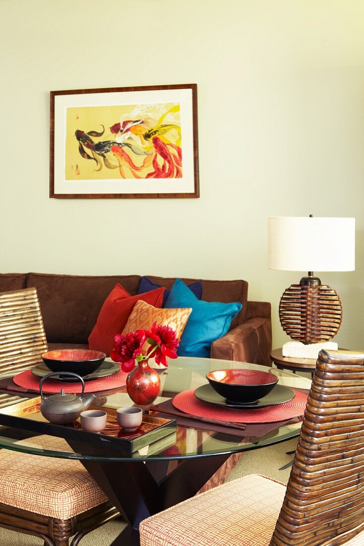 Round glass table with two Oriental place settings and comfortable sofa against wall below modern artwork