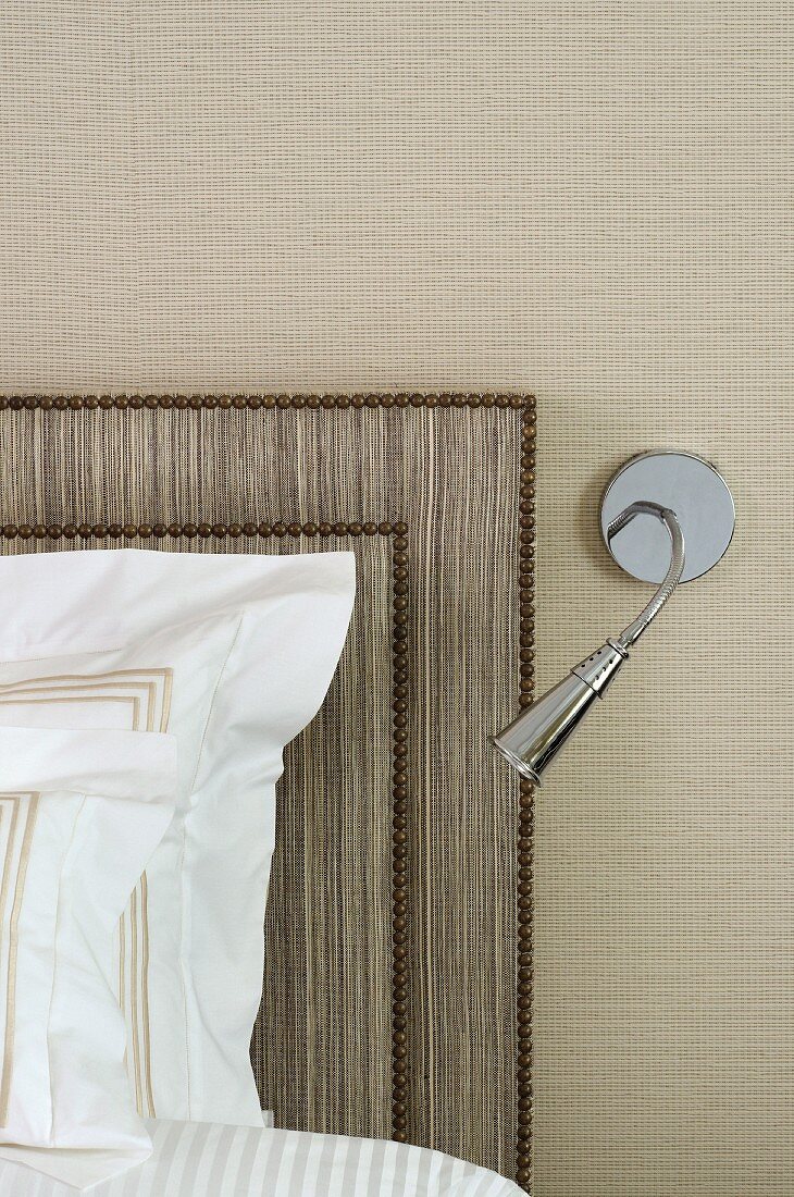 Modern, wall-mounted reading lamp next to bed with headboard