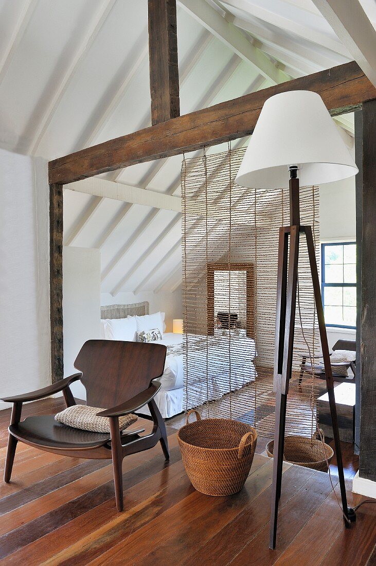 Sessel mit Holzgestell im Fiftiesstil und Vintage Stehleuchte vor transparentem Raumteiler zum Schlafbereich im Dachgeschoss