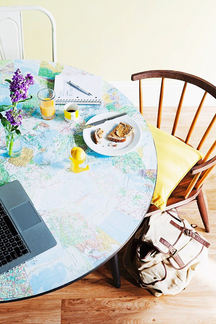 Im jugendlichen Stil aufgepeppter Frühstückstisch mit selbst aufgeklebter Weltkarte und Vintage Stühlen