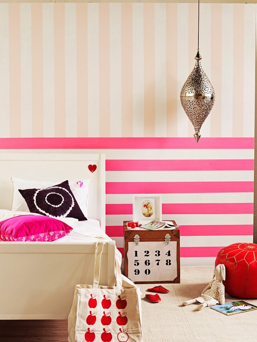 Hot pink horizontal stripes and pastel pink vertical stripes on wall behind rustic bed and chest used as bedside table in girl's bedroom