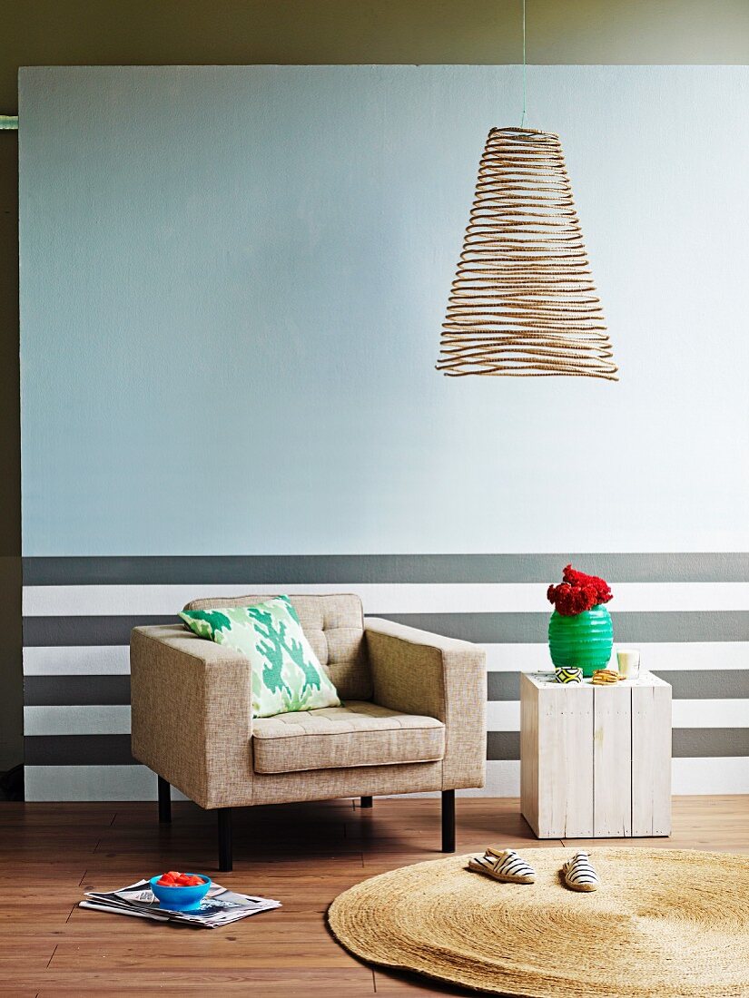 Insubstantial wire lampshade against pale wall; dado with grey horizontal stripes behind comfortable armchair