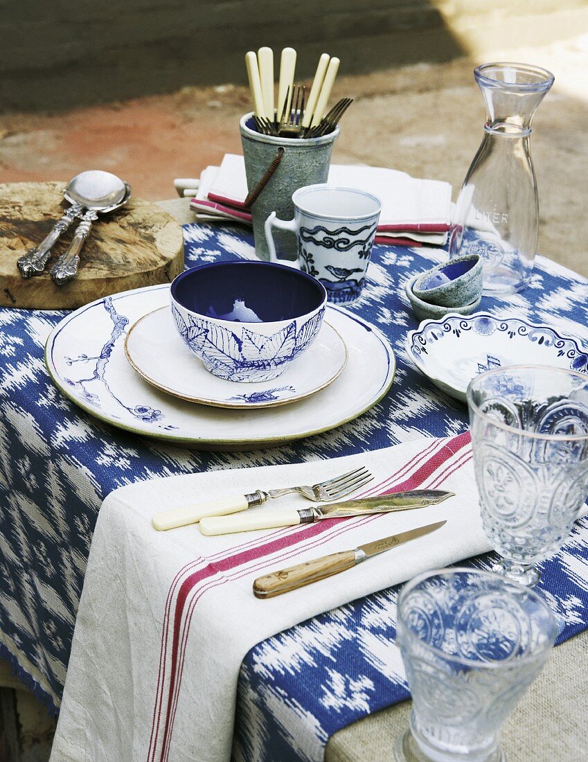 Place setting with blue and white painted bowl next to crystal glasses on white and blue patterned table runner