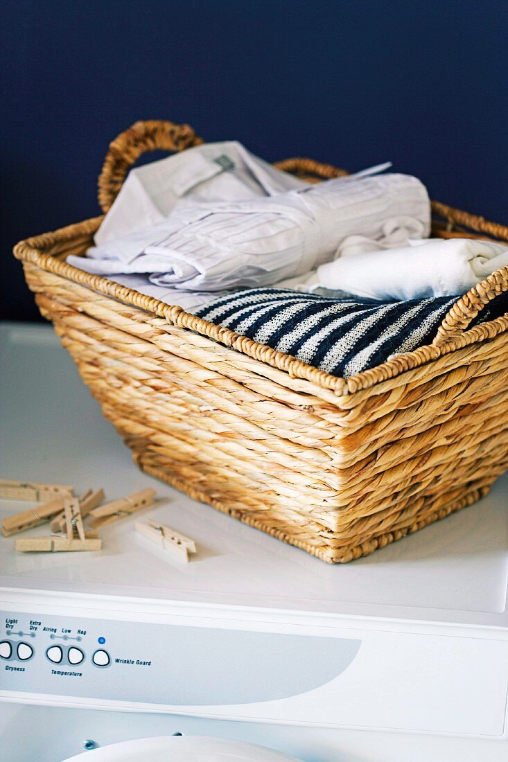 Laundry basket of fresh washing and clothes pegs on top of white washing machine