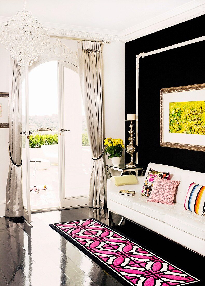 Teppichläufer in pink und weiss mit geometrischem Muster auf schwarzem Dielenboden vor weisser Couch und schwarze Wand in Wohnzimmerecke