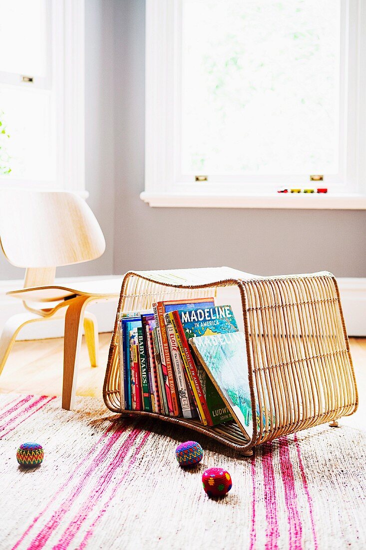 Korbregal auf dem Boden als Aufbewahrung für Bilderbücher; Kinderstuhl im Fiftiesstil und bunte Jonglierbälle