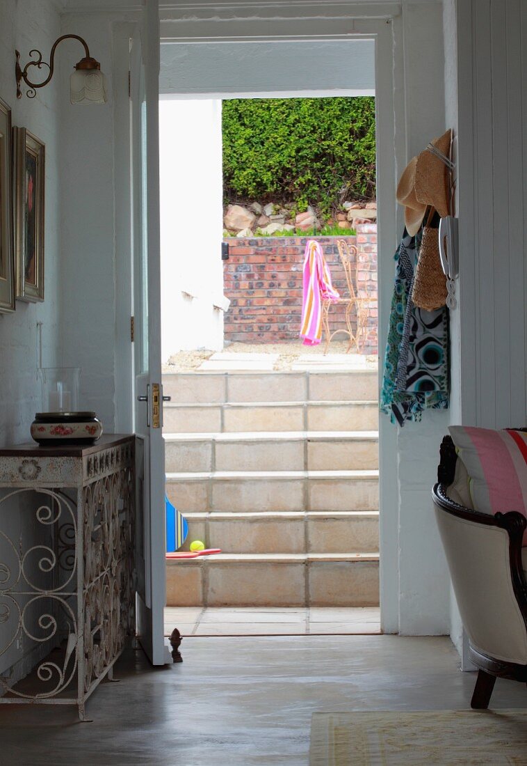 Offene Terrassentür und Blick auf geflieste Treppe vor Terrasse mit Bestuhlung neben Ziegelwand und Hecke