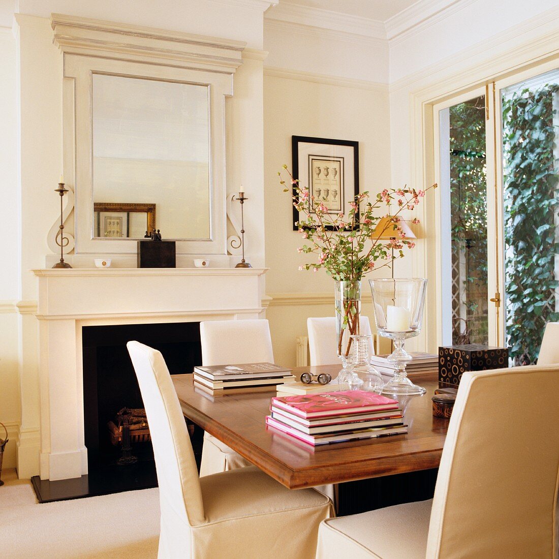 Stühle mit heller Husse und gestapelte Bücher auf Holztisch vor offenem Kamin in klassizistischem Wohnzimmer
