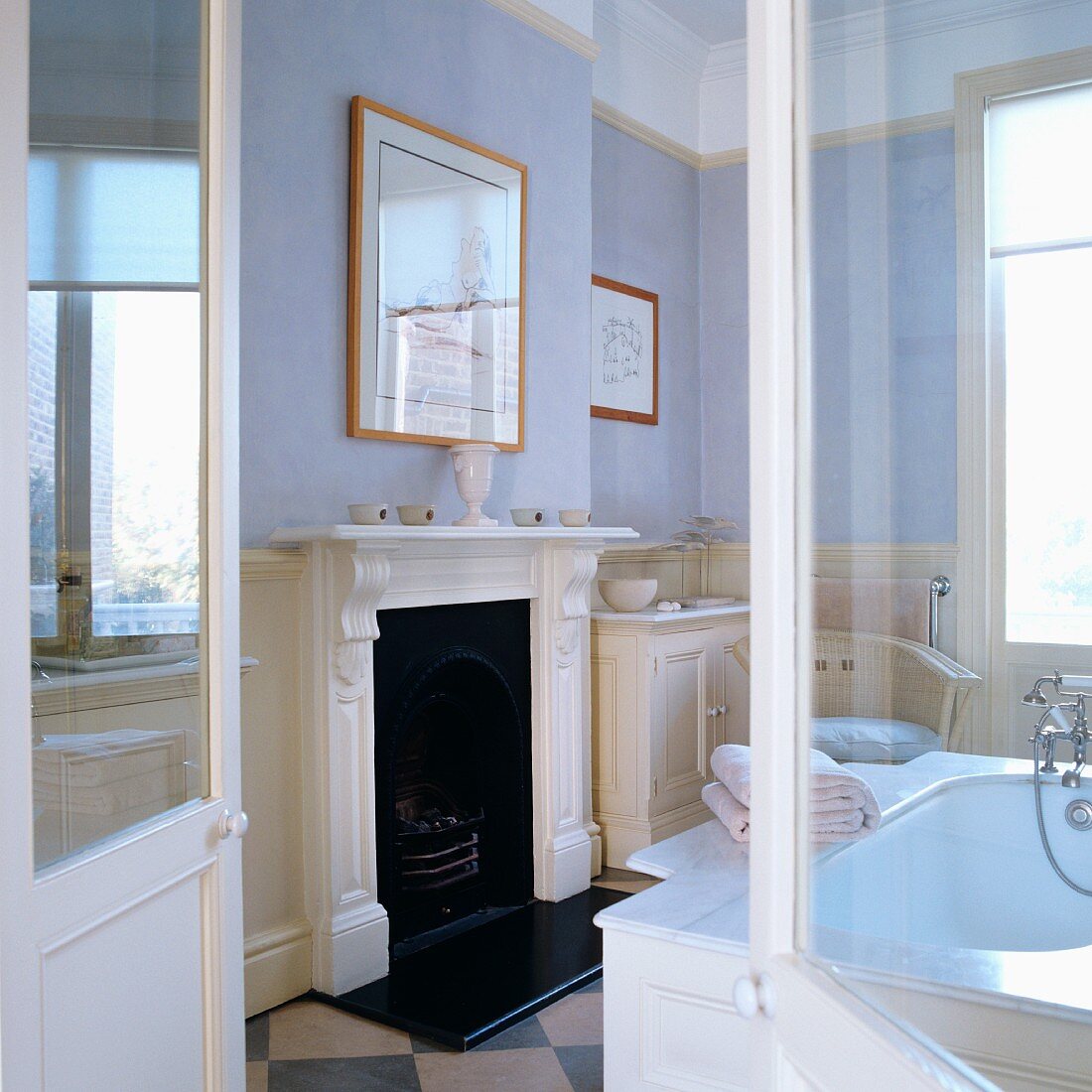 Blick durch offene Flügeltür auf Kamin mit weisser, profilierter Holzschürze in traditionellem Bad mit pastellfarben getönten Wänden