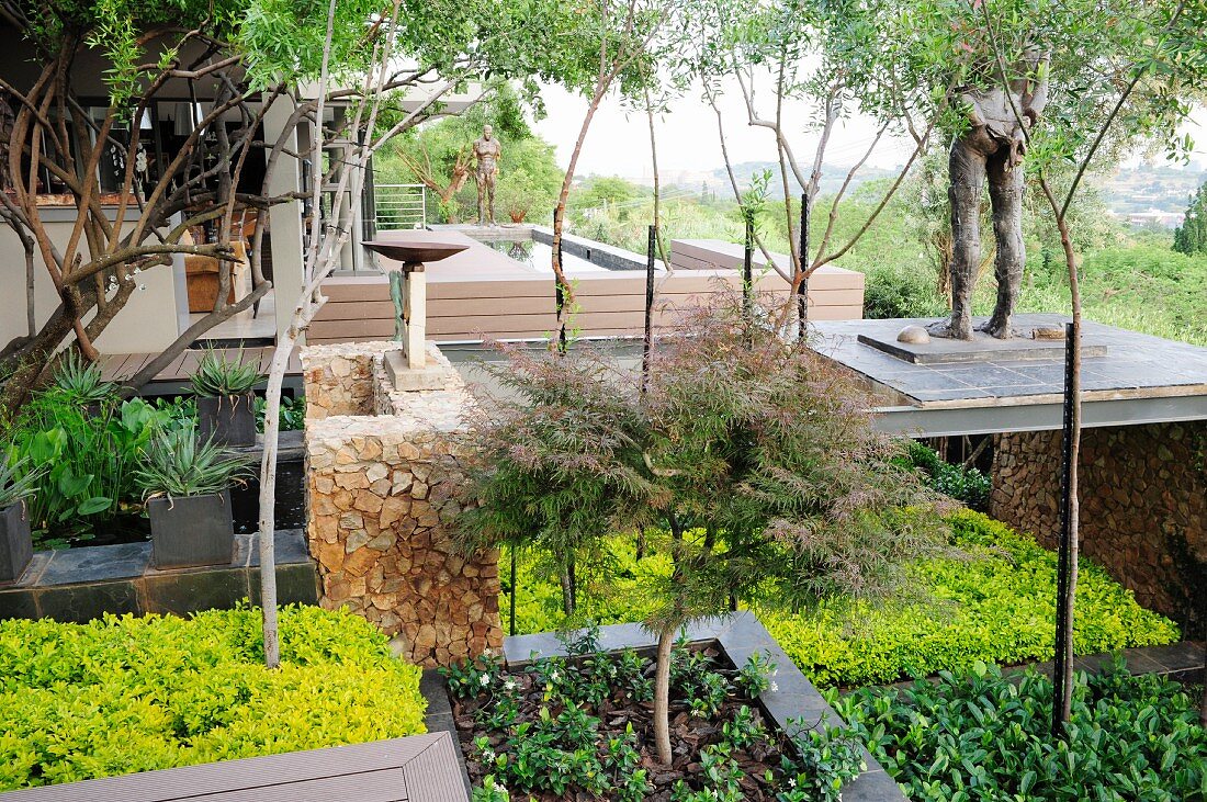 Terraced garden on slope with sculptures, beds and small trees
