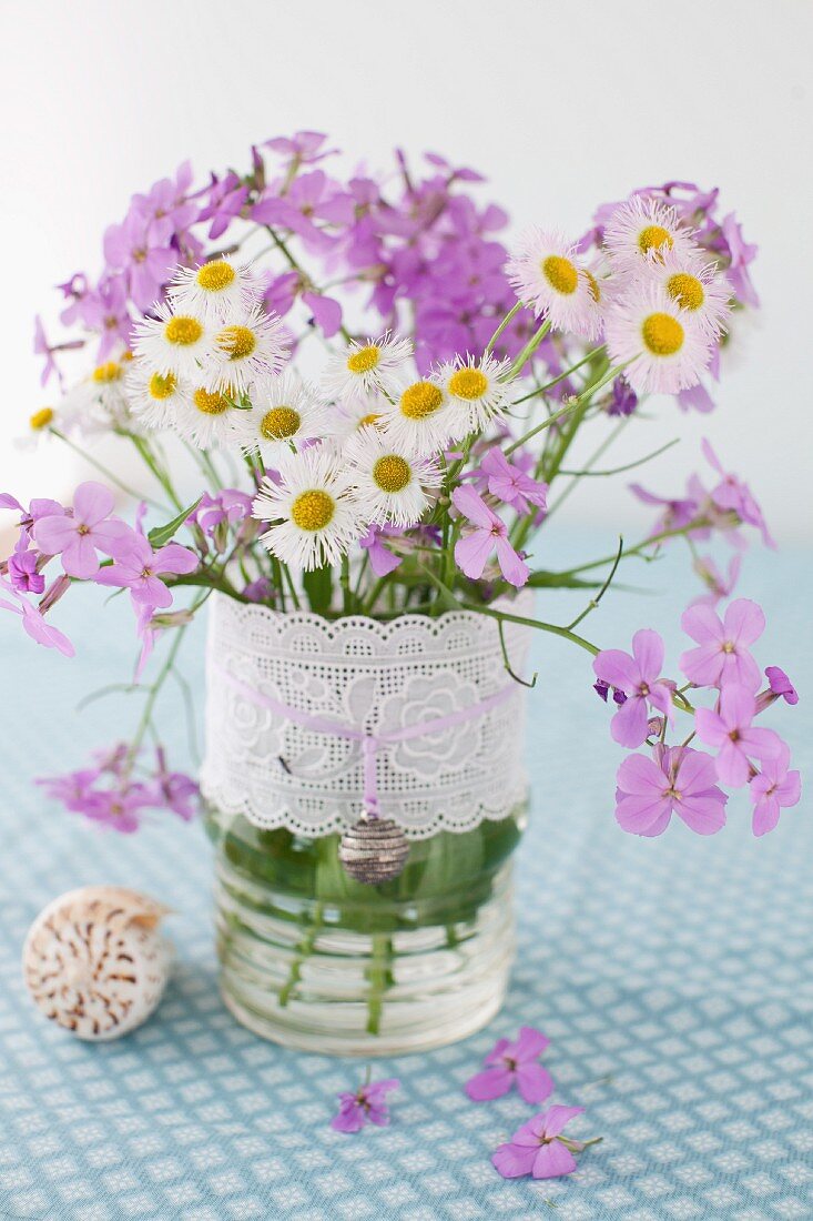 weiße und lila Wiesenblumen in einer Vase mit Spitzenborte