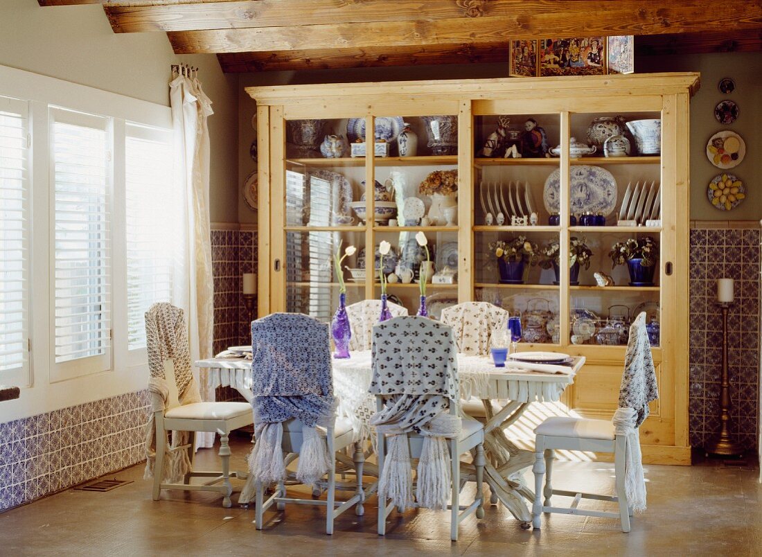 Chairs with fabric draped on backs around dining table in front of dresser full of crockery