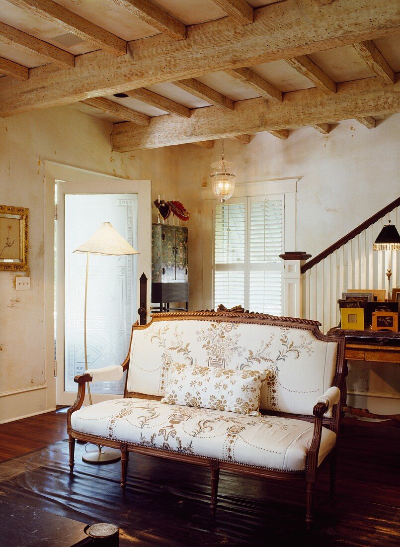 Antike Sitzbank mit floralem Muster im Wohnraum mit rustikaler Holzbalkendecke