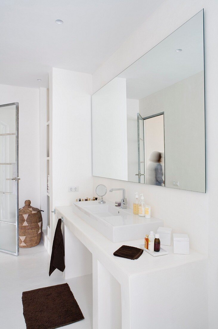 Minimalist white bathroom with large mirror above washstand and dark, contrasting towels