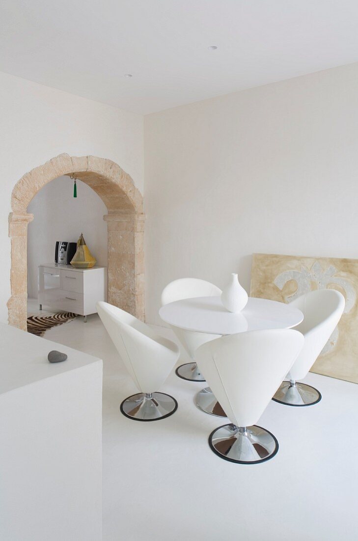 Essplatz mit Designer Schalensitzen in weißem minimalistischem Zimmer mit historischem Rundbogendurchgang