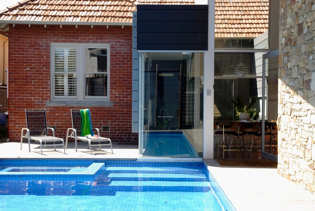Renoviertes Wohnhaus mit einer Fassadenabfolge von Ziegel, Glas und Naturstein; Übergang von Gartenpool in Innenschwimmbecken
