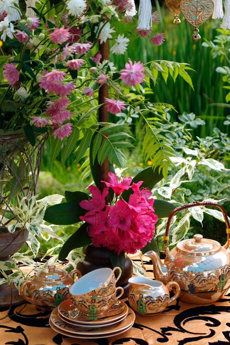 Old, Chinese, porcelain tea set surrounded by luxuriantly flowering plants