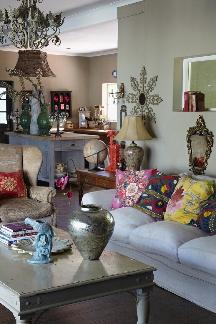 Silberne Vase auf Couchtisch und folkloristische Kissen auf Sofa in offenem Wohnraum, im Hintergrund der Küchenbereich