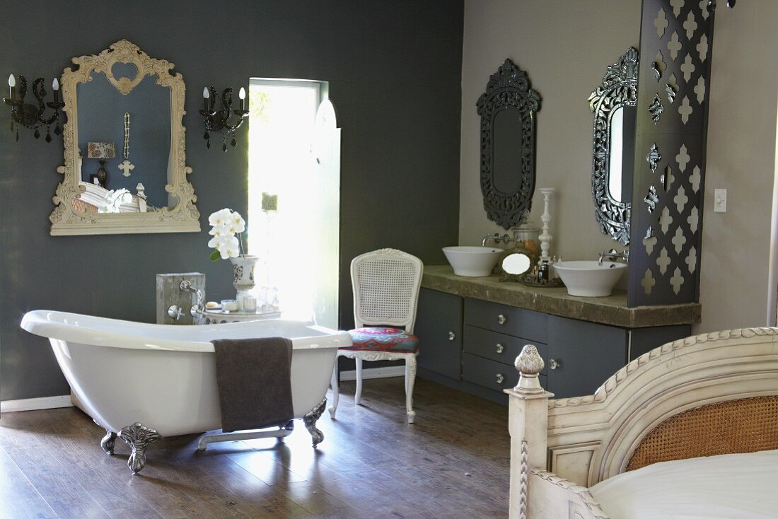 Free-standing vintage bathtub in front of grey wall and mirror with carved frame in spacious bathroom
