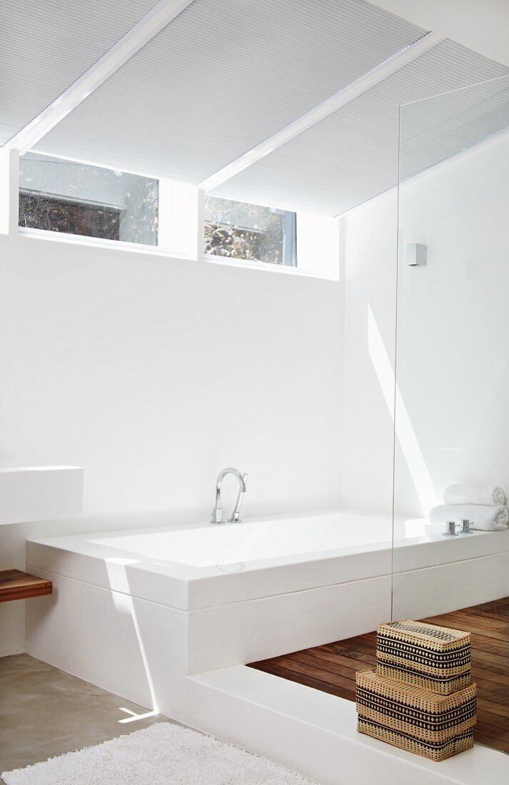 Designerbad mit Badewanne auf Podest gegenüber Duschbereich mit Glasabtrennung