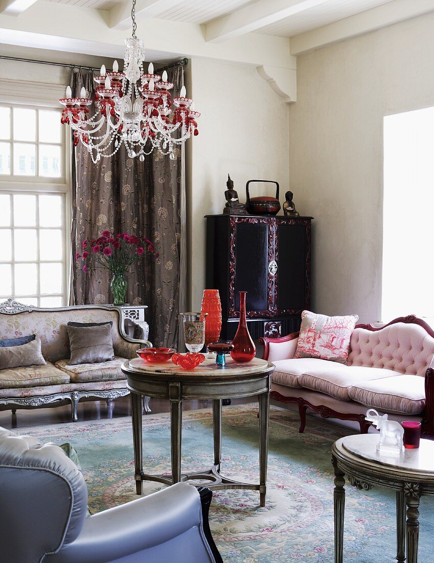 Antique sofas and pretty crystal chandelier above round side table in romantically inspired interior