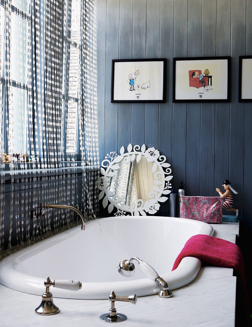 Bathtub with retro tap fittings in marble surround; pictures from Tintin comics on blue-stained wall cladding