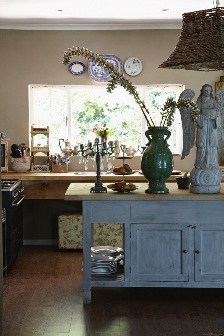 Angel statue next to green vase of flowering branches on vintage wooden sideboard in open-plan kitchen
