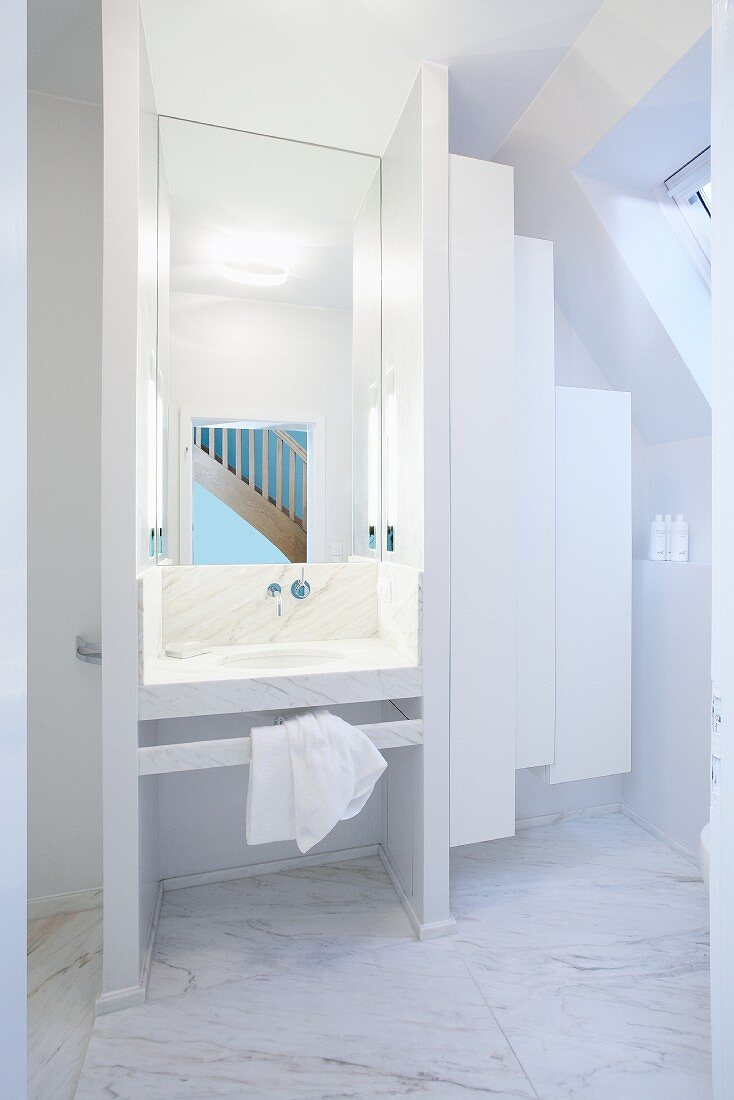 White designer bathroom - screened marble washstand next to white suspended cupboards below sloping ceiling