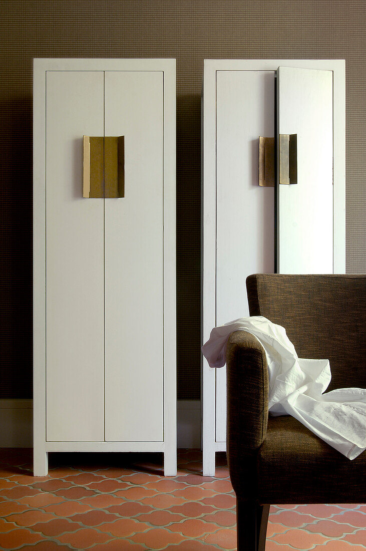 Two white, designer wardrobes with brass door handles on terracotta floor tiles