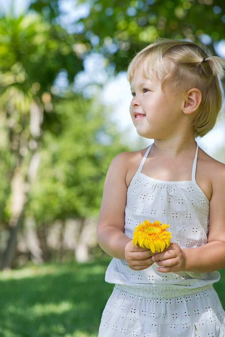 Little, blonde girl with a flower in the garden