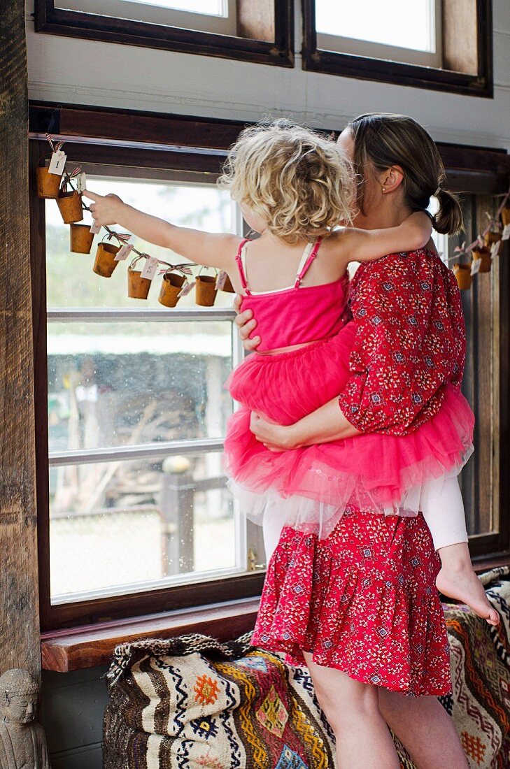 Mutter mit Tochter vor selbstgemachter Adventskalender-Girlande am Fenster