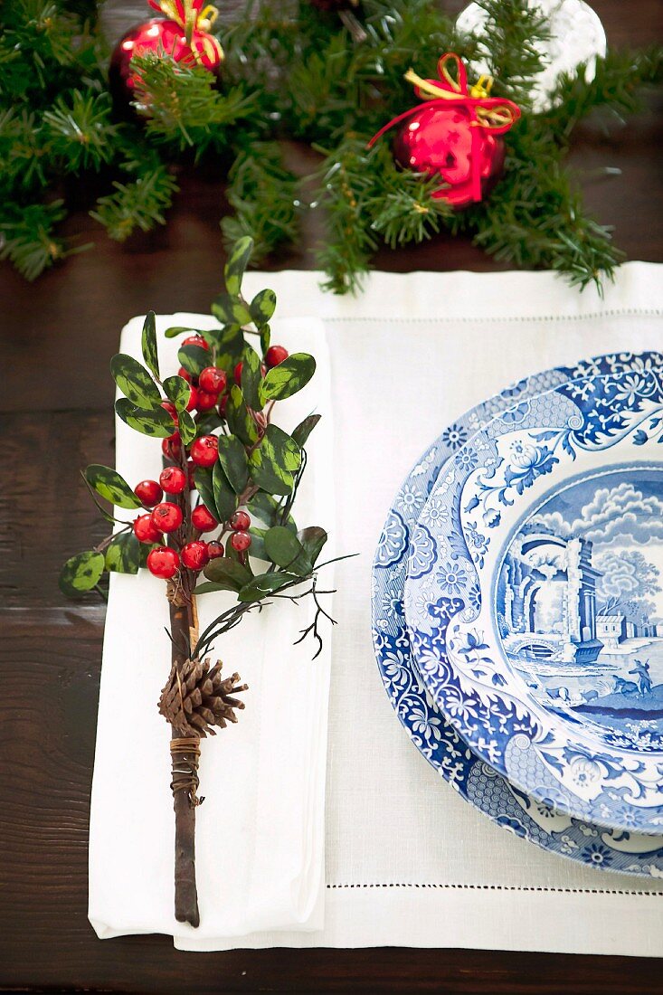 Place setting with blue and white crockery on pulled thread work place mat and small posy with pinecone and red berries as festive table decoration