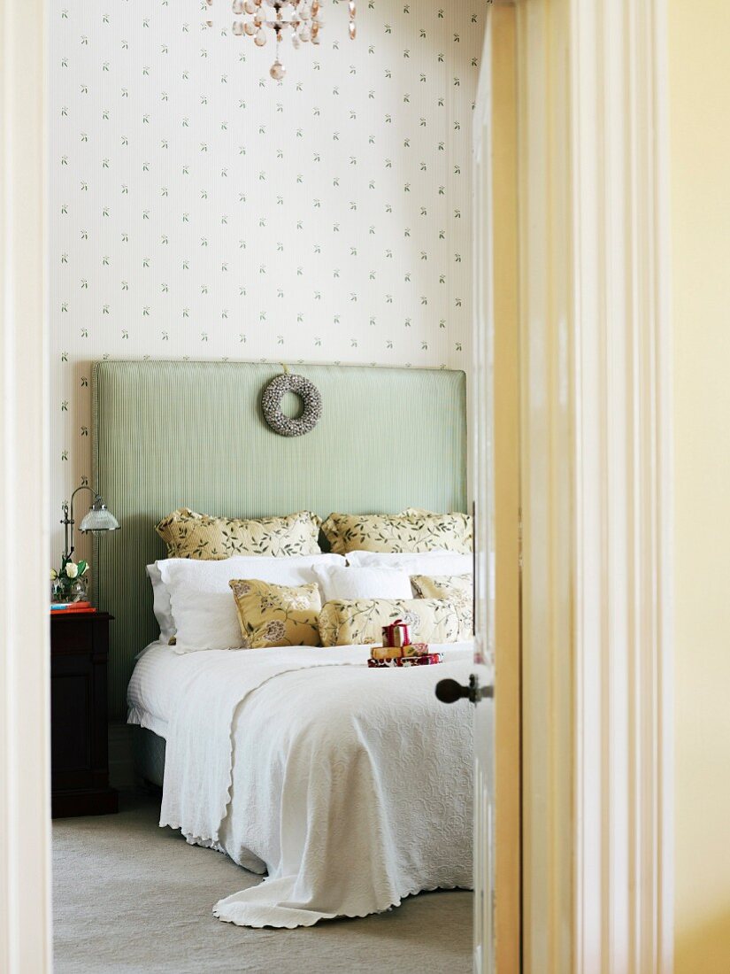 Blick durch die offene Schlafzimmertür auf Doppelbett mit gepolstertem Kopfende in Pastellgrün, geschmückt mit einem Silberkranz