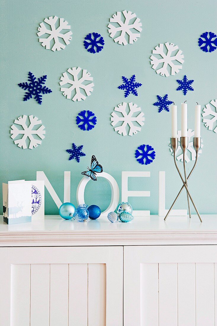 weiße und blaue, stilisierte Eisblumen an der Wand über einer Kommode mit Weihnachtsdeko