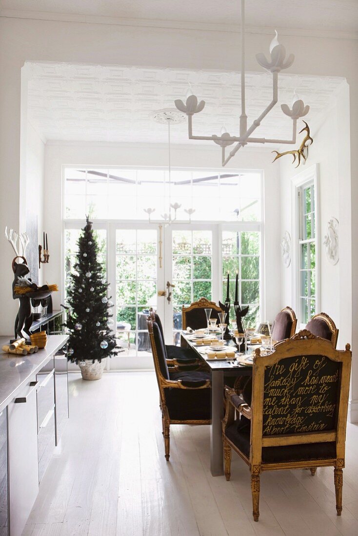 Armchairs with writing in gold on backs at festively set dining table; decorated Christmas tree in background