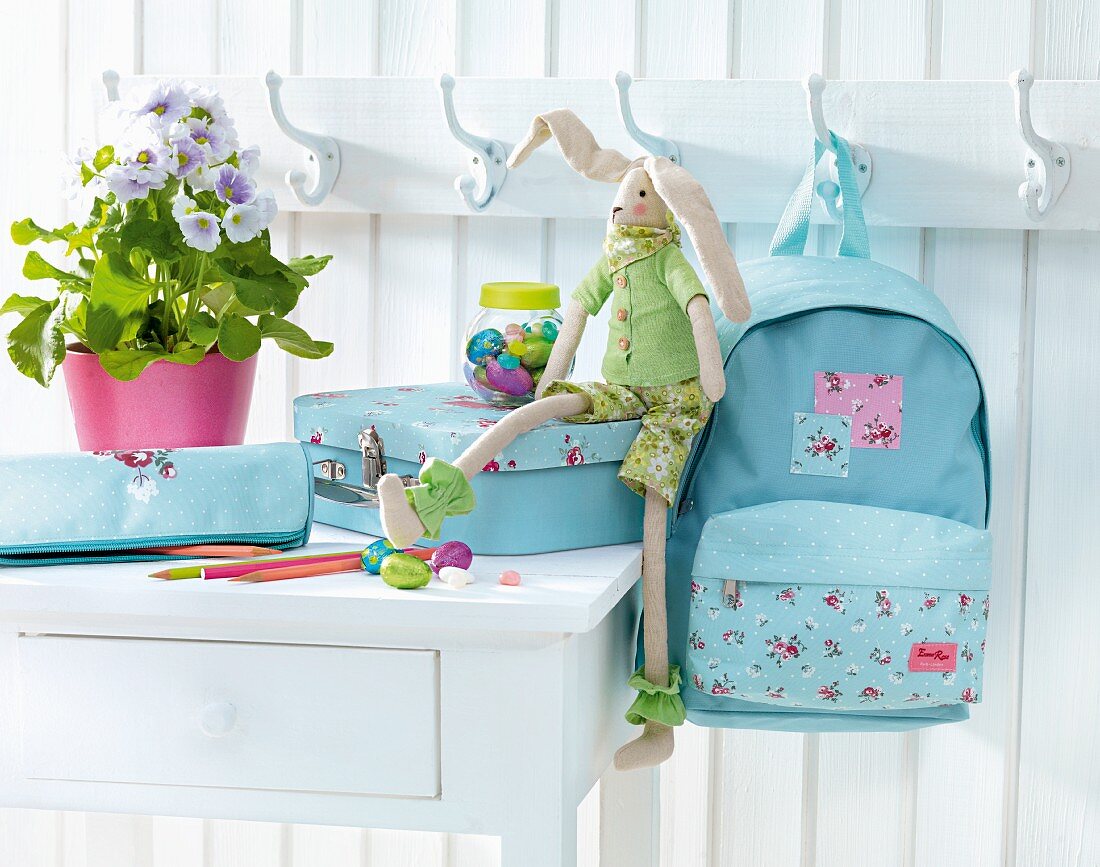 Child's bag set on white table and hanging on coat rack on white wooden wall