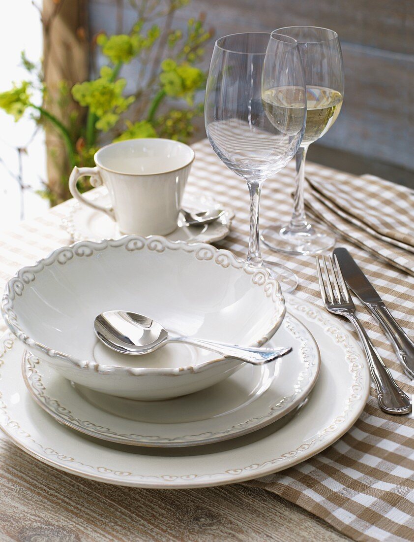 Tableware with a soup bowl and wine glasses on a checked tablecloth